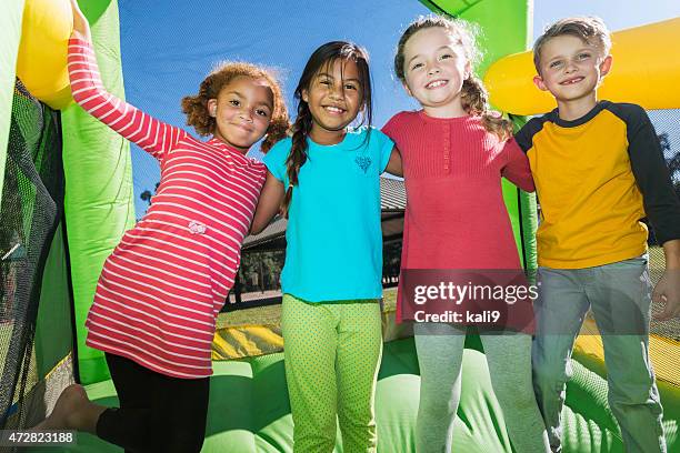 four multi-ethnic children playing on bouncy castle - bounce castle stock pictures, royalty-free photos & images