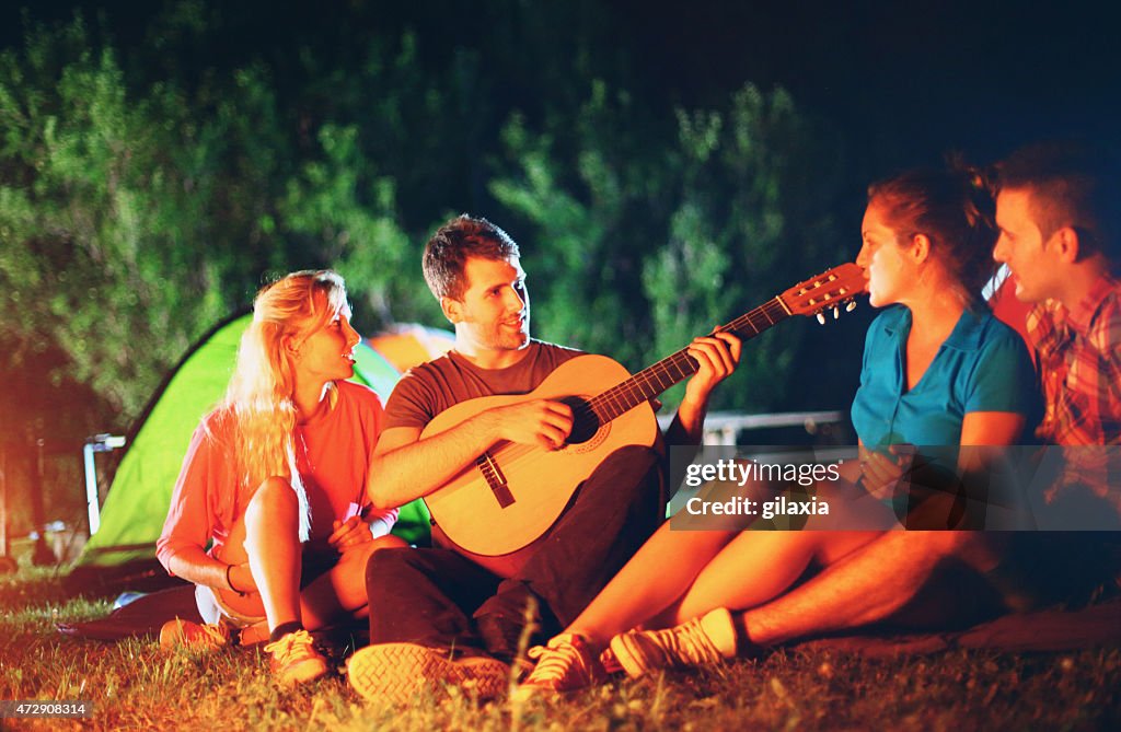 Friends playing guitar by campfire.