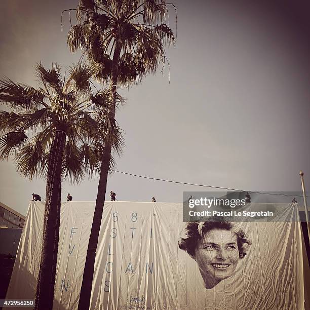 Workers are seen as they install the official poster of the 68th Cannes Film Festival on the facade of the Palais des Festivals on May 11, 2015 in...