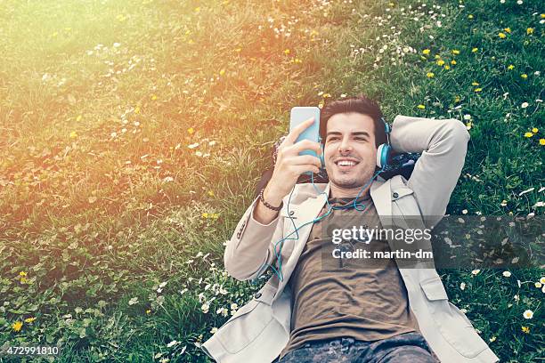 man in the park listening to the music from smartphone - young man listening to music on smart phone outdoors stockfoto's en -beelden