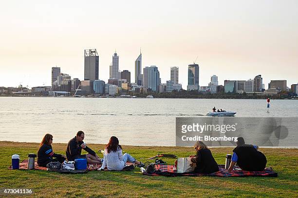 People picnic on the bank of the Swan River as commercial buildings stand in the business district in Perth, Australia, on Sunday, May 10, 2015....