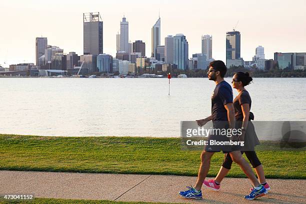 People walk along the bank of the Swan River as commercial buildings stand in the business district in Perth, Australia, on Sunday, May 10, 2015....