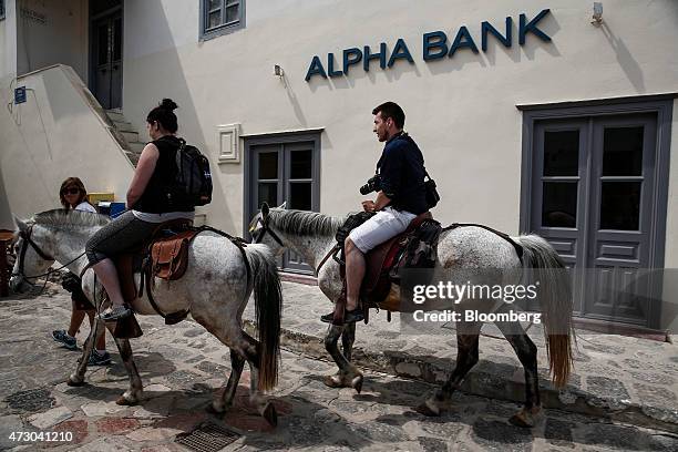 Tourists ride horses past an Alpha Bank AE bank branch on the island of Hydra, Greece, on Monday, May 11, 2015. Less than three weeks after a Greek...