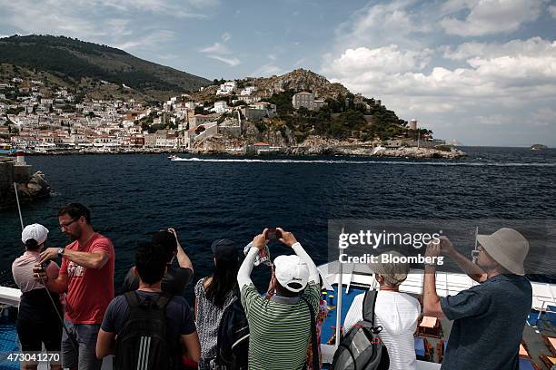 Tourists stand on deck to take photographs as they approach the island of Hydra aboard a cruise ship sailing in the Saronic gulf in Hydra, Greece, on...