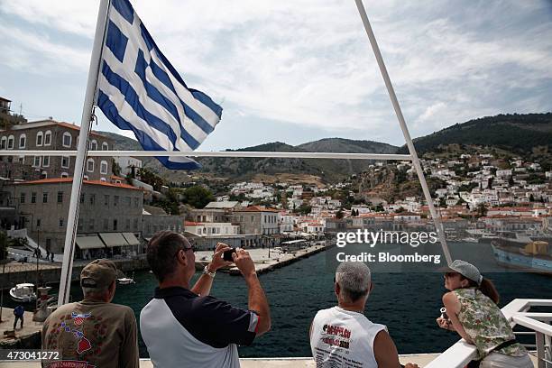 Tourists stand on deck to take photographs as they approach the island of Hydra aboard a cruise ship sailing in the Saronic gulf in Hydra, Greece, on...