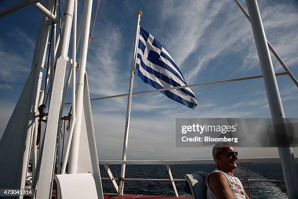 Tourist sits in the sun beside a Greek national flag aboard a cruise ship sailing in the Saronic gulf west of Athens, Greece, on Monday, May 11,...