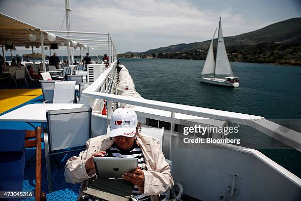 Tourist wearing an "I Love Greece" cap checks her Apple Inc. IPad as she sails aboard a cruise ship in the Saronic gulf, west of Athens, Greece, on...