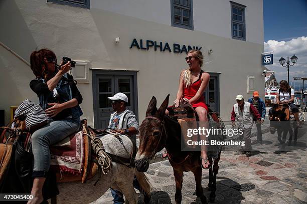 Tourists enjoy a donkey ride as they pass an Alpha Bank AE bank branch while visiting the island of Hydra, Greece, on Monday, May 11, 2015. Less than...