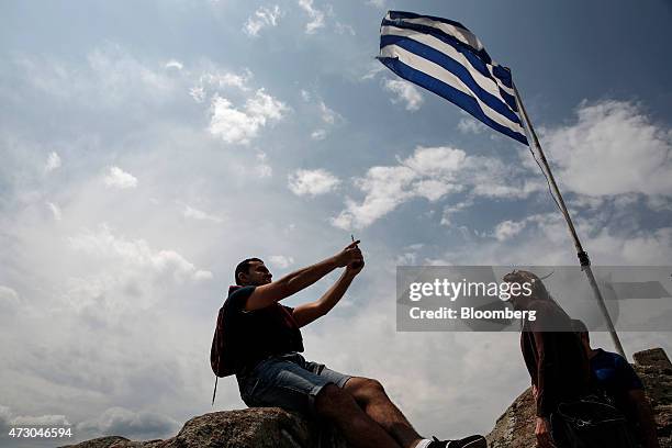 Tourists pose for photographs beneath a Greek national flag during a visit to the island of Poros, Greece, on Monday, May 11, 2015. Less than three...