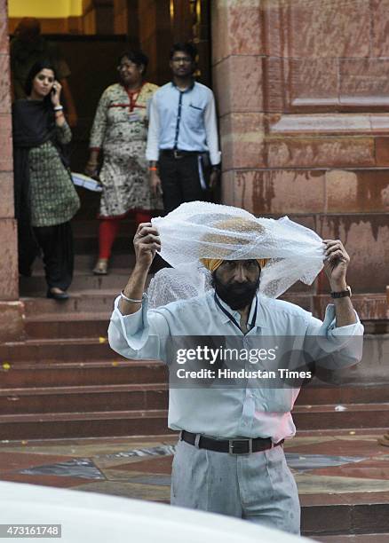 An sikh employee cover his head with a plastic sheet to protect him self from the rain at Parliament on the concluding day of Budget session on May...