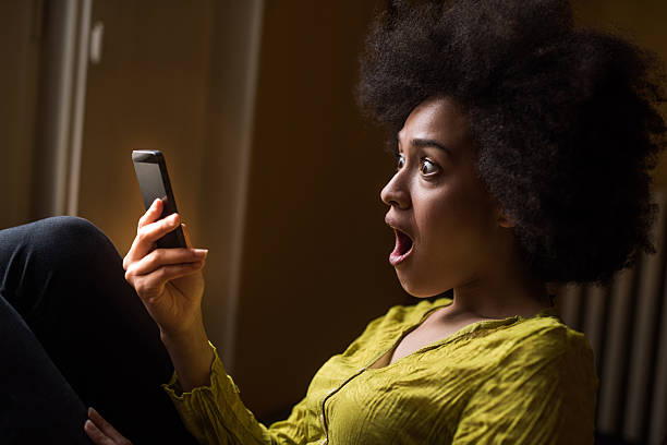 african american woman received a shocking text message. - black woman phone shock stock pictures, royalty-free photos & images