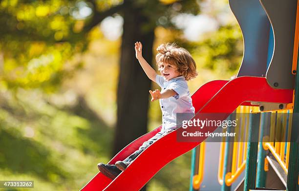 cheerful little boy having fun while sliding outdoors. - children's slide stock pictures, royalty-free photos & images