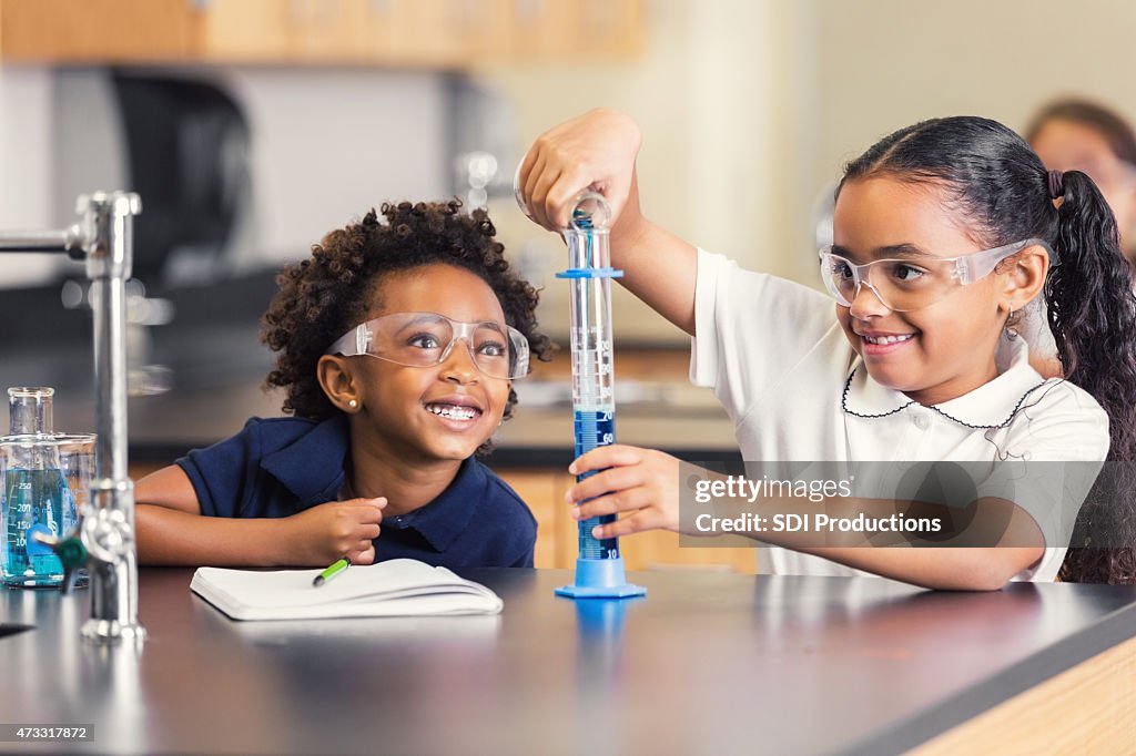 Cute elementary students smiling while doing science experiment in class