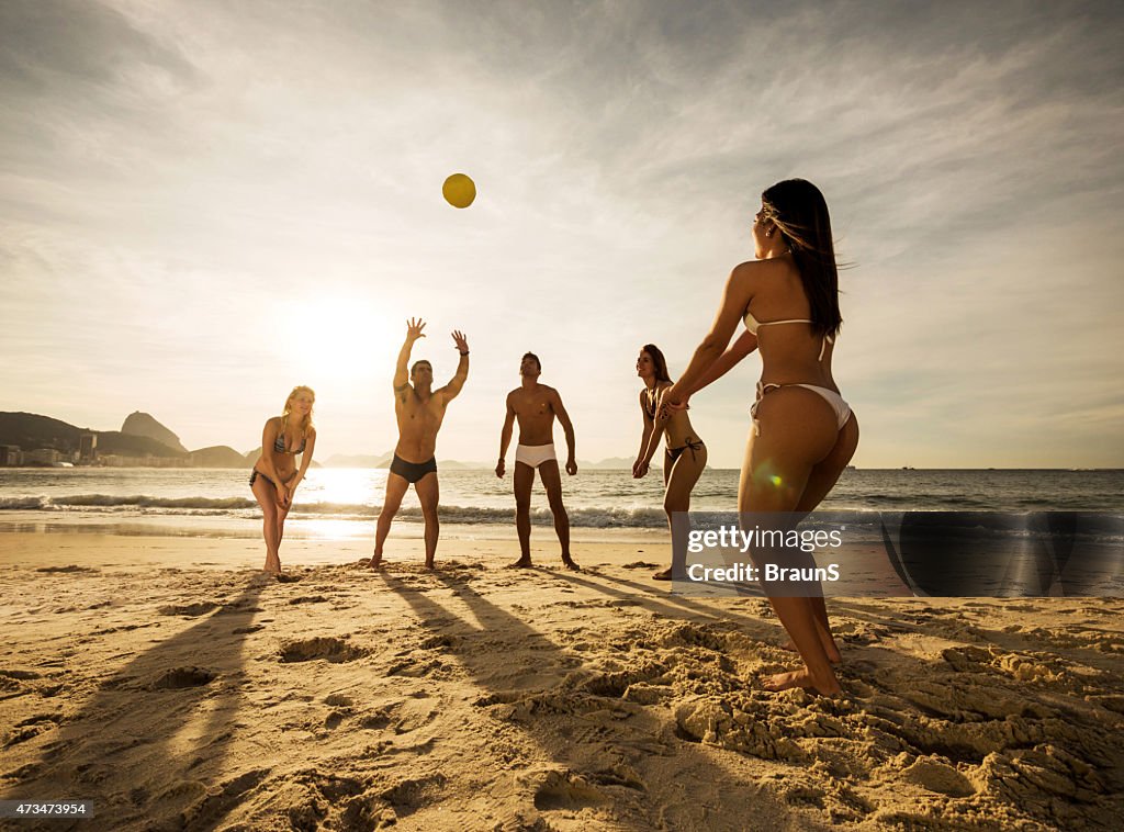 Gruppo di giovani giocare a beach volley al tramonto.