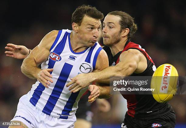 Brent Harvey of the Kangaroos handballs whilst being tackled by Travis Colyer of the Bombers during the round seven AFL match between the Essendon...