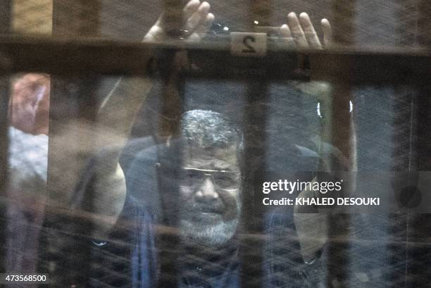 Egypt's deposed Islamist president Mohamed Morsi raises his hands from behind the defendant's cage as the judge reads out his verdict sentencing him...