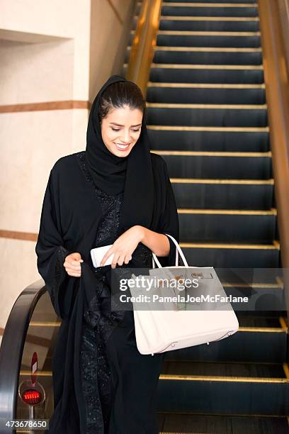 traditionally dressed middle eastern woman stepping off hotel escalator - black purse stock pictures, royalty-free photos & images