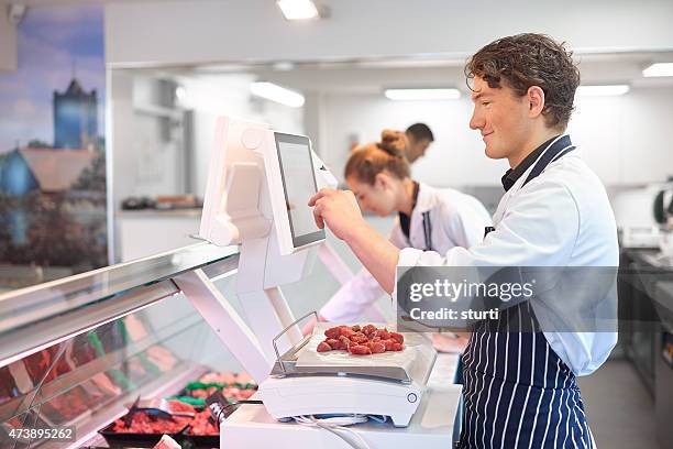 young male and female butchers working in a butcher's shop. - butcher stock pictures, royalty-free photos & images