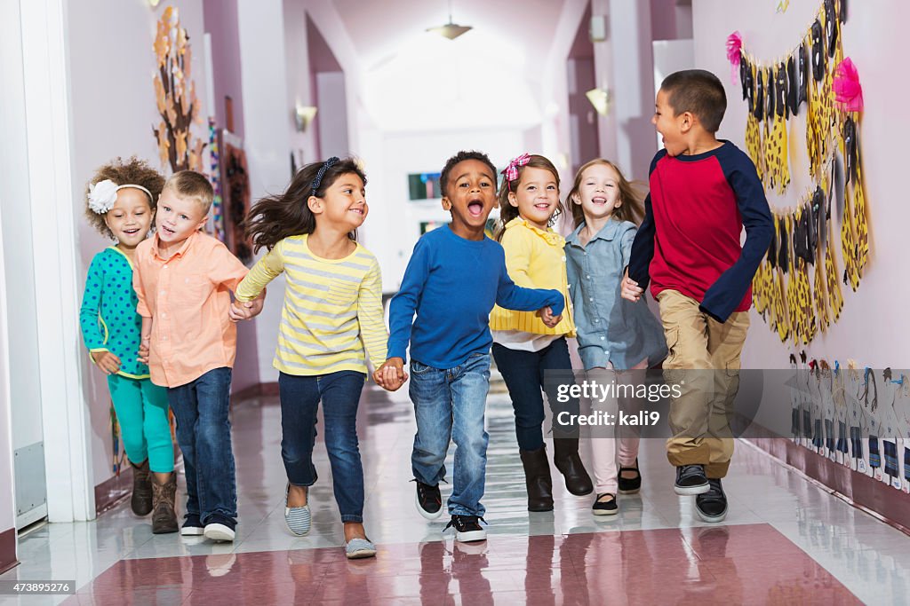 Multiracial group of preschoolers running down hallway