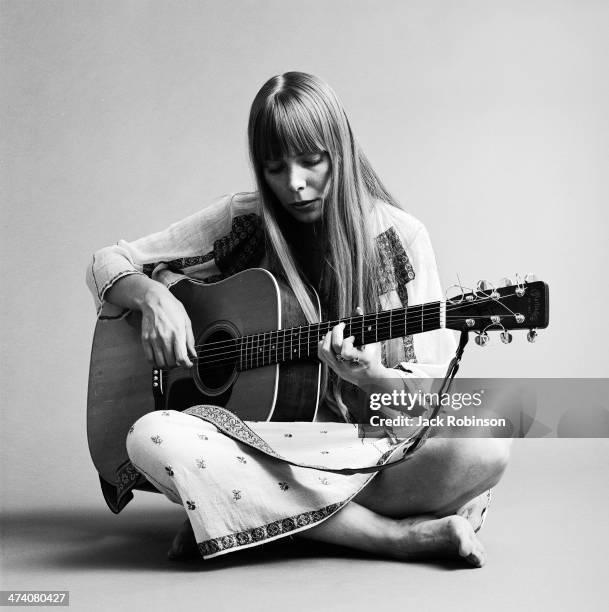 Portrait of Canadian musician Joni Mitchell seated on the floor playing acoustic guitar, November 1968. This image is from a shoot for the fashion...