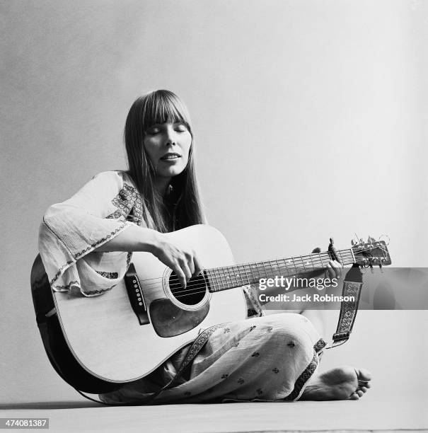 Portrait of Canadian musician Joni Mitchell seated on the floor playing acoustic guitar, November 1968. This image is from a shoot for the fashion...