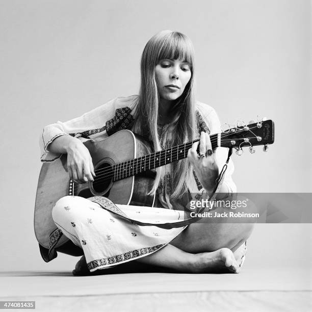 Portrait of Canadian musician Joni Mitchell seated on the floor playing acoustic guitar, November 1968. This image is from a shoot for the fashion...