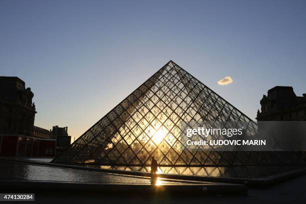 Man walks at sunset in front of the Louvre Pyramide on May 20, 2015 in Paris. AFP PHOTO / LUDOVIC MARIN