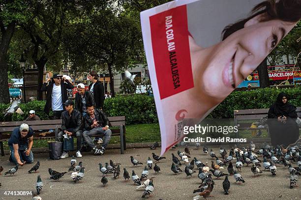 People feed pigeons next to a poster of political party 'Barcelona en Comu' Leader Ada Colau are seen during a Municipal Elections rally on May 20,...