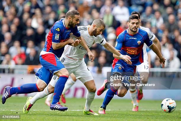 Karim Benzema of Real Madrid competes for the ball with David Lomban and Alberto Botia of Elche during the La Liga match between Real Madrid and...