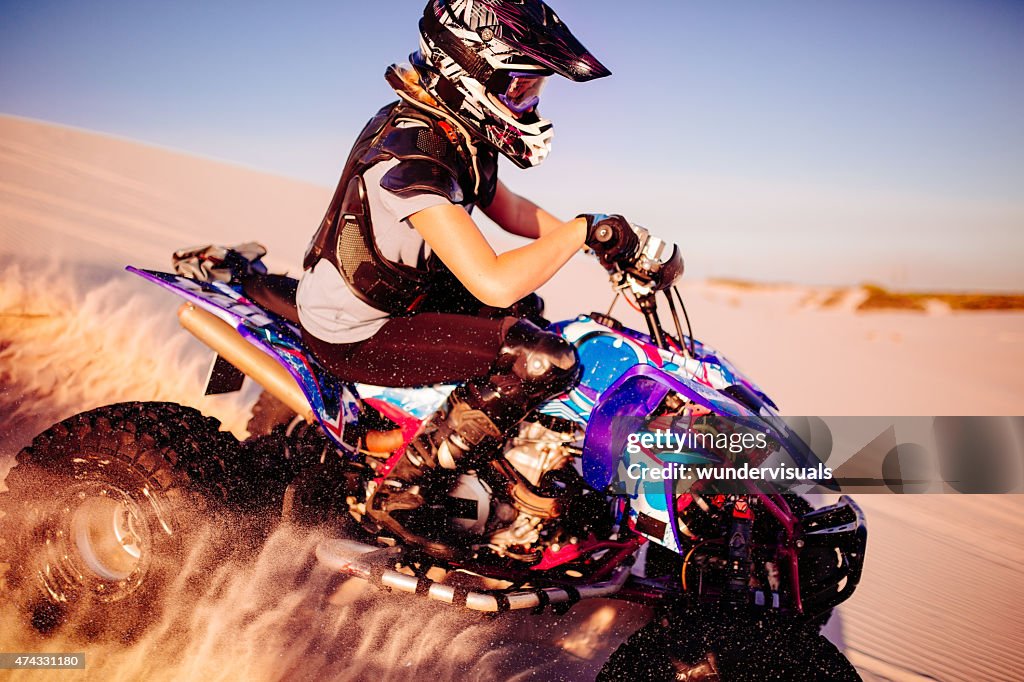 Girl quad racer in protective gear racing over sand dunes