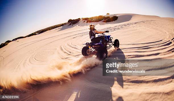 professional quad biker kicking up sand on a dune - extreme sports bike stock pictures, royalty-free photos & images