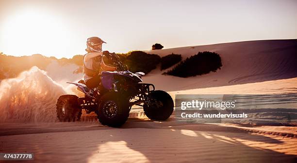 quad bike racer in protective gear driving on sand dunes - quad bildbanksfoton och bilder