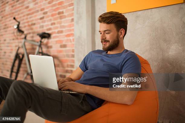 man sitting in bean bag and using laptop. - bean bags stock pictures, royalty-free photos & images