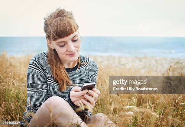 red-haired woman texting by the sea - woman smartphone nature stockfoto's en -beelden