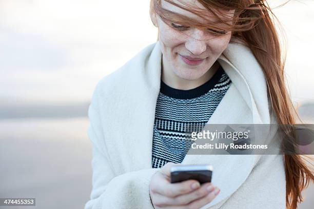 red-haired woman texting on beach - world at your fingertips stockfoto's en -beelden