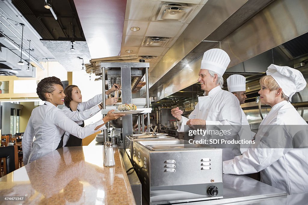 Cozinheiros e waitstaff trabalhar em conjunto em bancas cozinha de Restaurante