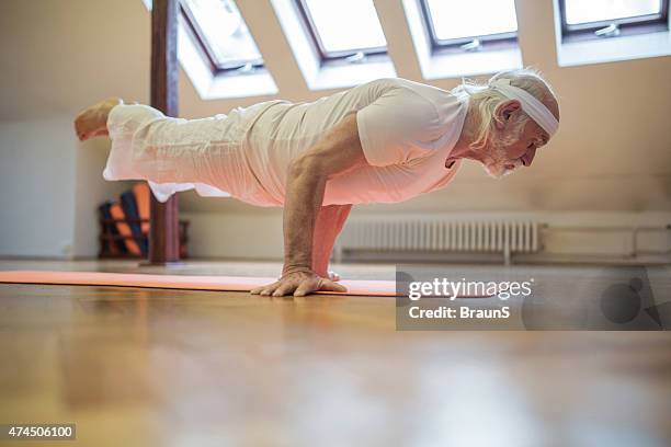 alter mann ausübung yoga, während sie sich in der peacock pose. - senior yoga stock-fotos und bilder