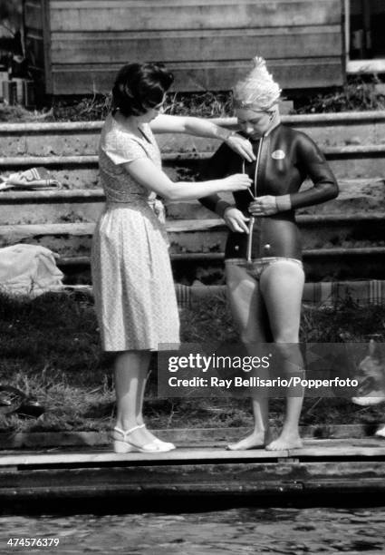 Queen Elizabeth II helping her sister, Princess Margaret, into a wetsuit prior to water-skiing at Sunninghill Park, Windsor on 25th July 1964. This...