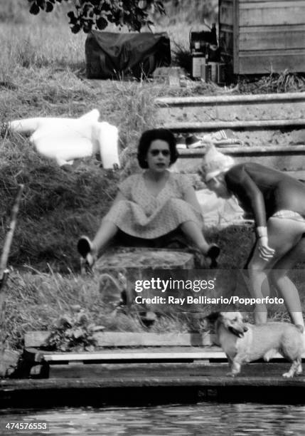 Queen Elizabeth II watches whilst her sister Princess Margaret, wearing a wetsuit, prepares to water-ski at Sunninghill Park, Windsor on 25th July...