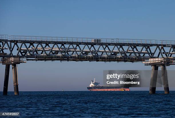 Fuel pipes stand raised over the Mediterranean Sea on a jetty as a cargo ship passes beyond at the VTTV oil storage terminal, a joint venture of...