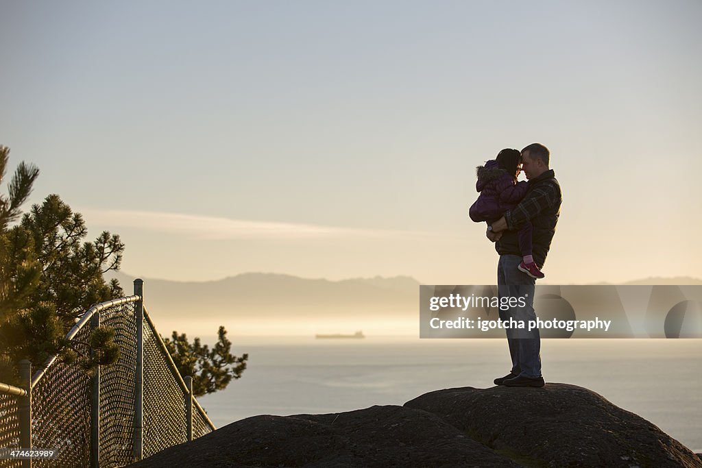 Father and Daughter hugging on rock at sunset