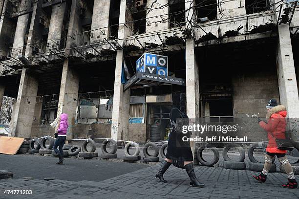 People walk past a burnt out building in Independence Square where dozens of protester were killed in clashes with riot police last week on February...