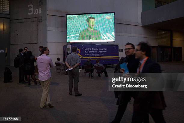 Attendees watch a television screen broadcasting the keynote address of Mark Zuckerberg, chief executive officer of Facebook Inc., on the opening day...