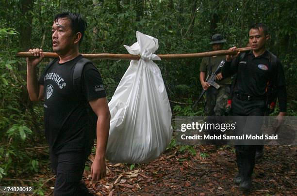 Malaysia police forensic team carry unidentified human remains down from a mass grave site suspected to be of ethnic Rohingyas between the...