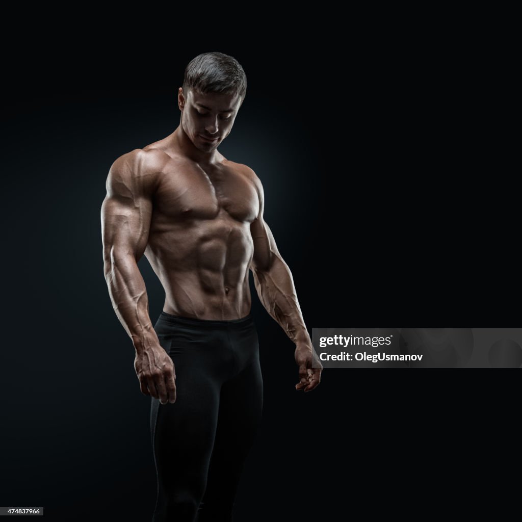 Fit young bodybuilder posing over black background