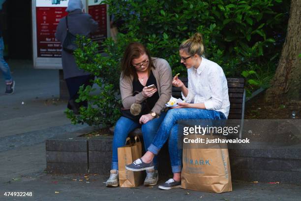 two caucasian women with mobiles and pommes frites - chips essen stock pictures, royalty-free photos & images