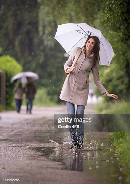 beautiful woman dancing in the rain with umbrella, puddle fun - female fashion with umbrella stock pictures, royalty-free photos & images