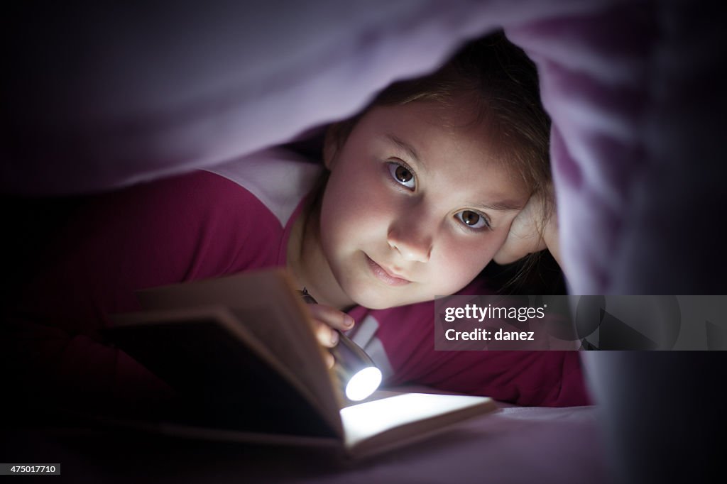 Girl reading under sheet using flashlight