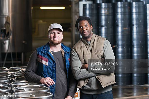 two men standing in storage warehouse with steel drums - craft brewery stock pictures, royalty-free photos & images