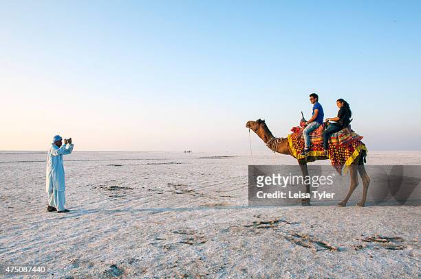 Local guide taking picture of tourists astride a camel in the Great Rann of Kutch, a seasonal salt marsh located in the Thar Desert of Gujarat, India...
